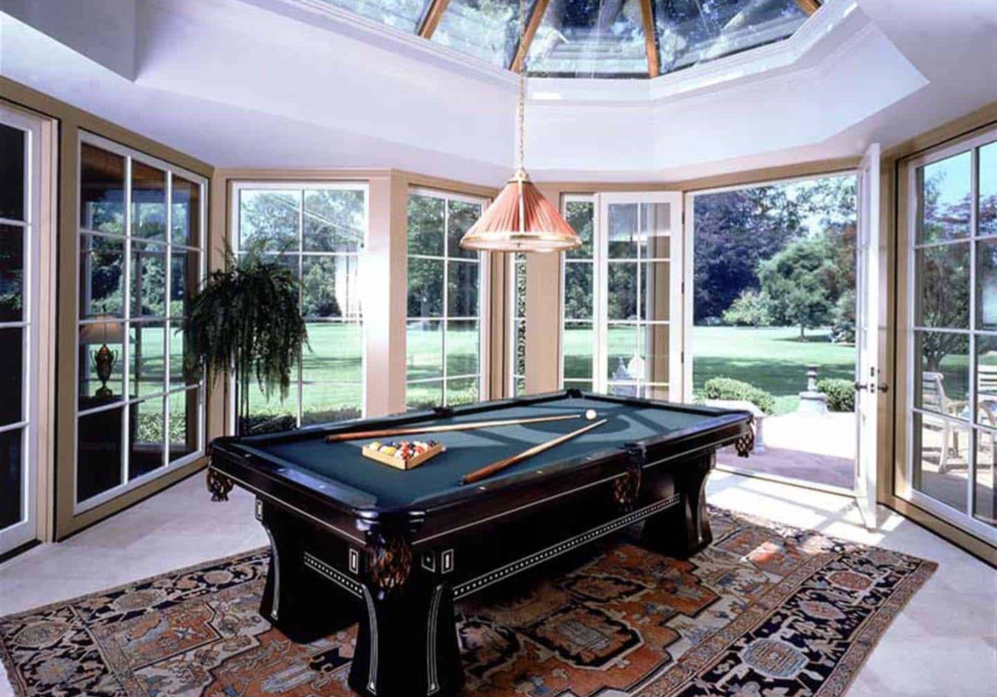 Billiards table on a rug in room with only windows and a skylight.